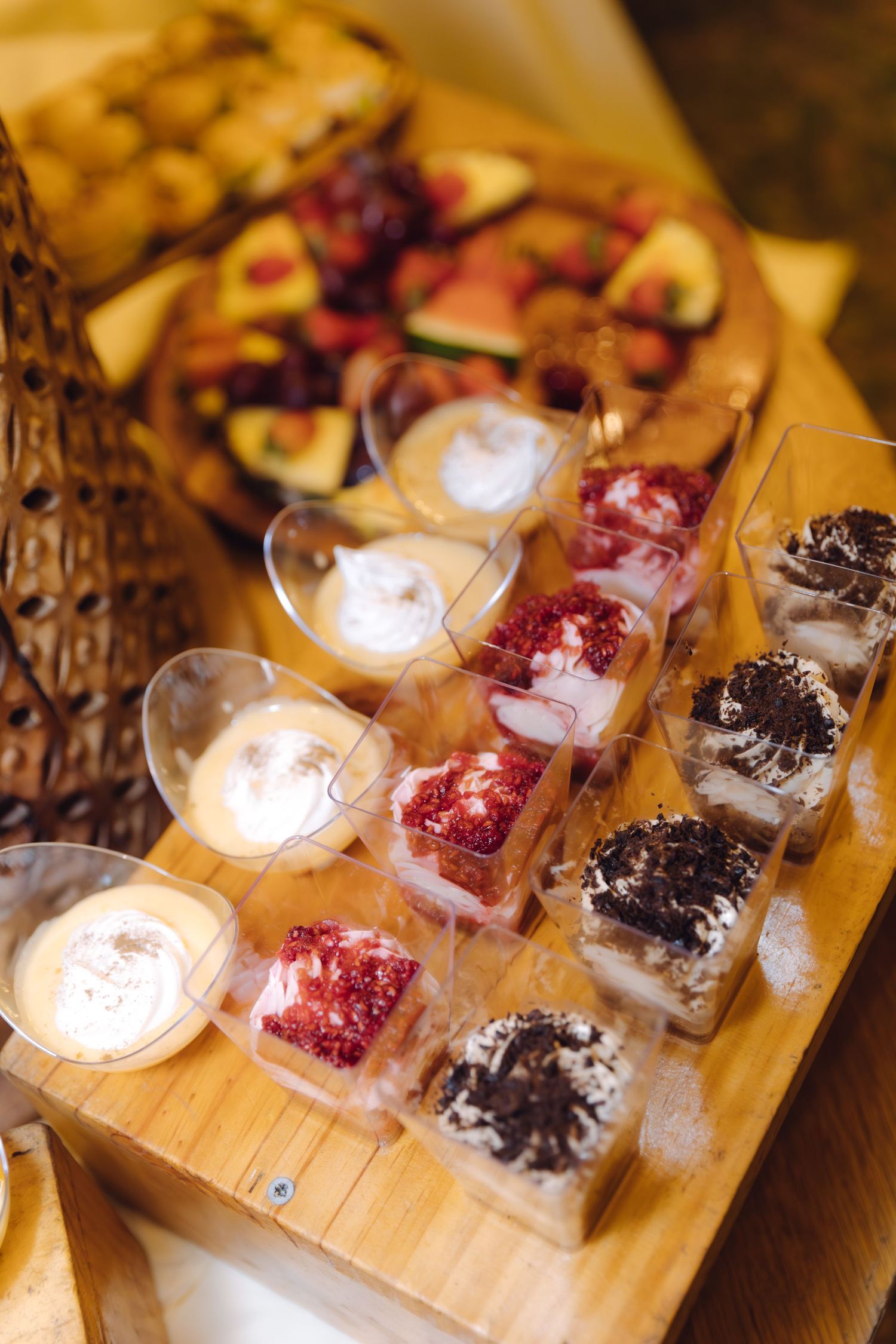 Assorted wedding dessert cups with strawberry and chocolate trifles on wooden board.