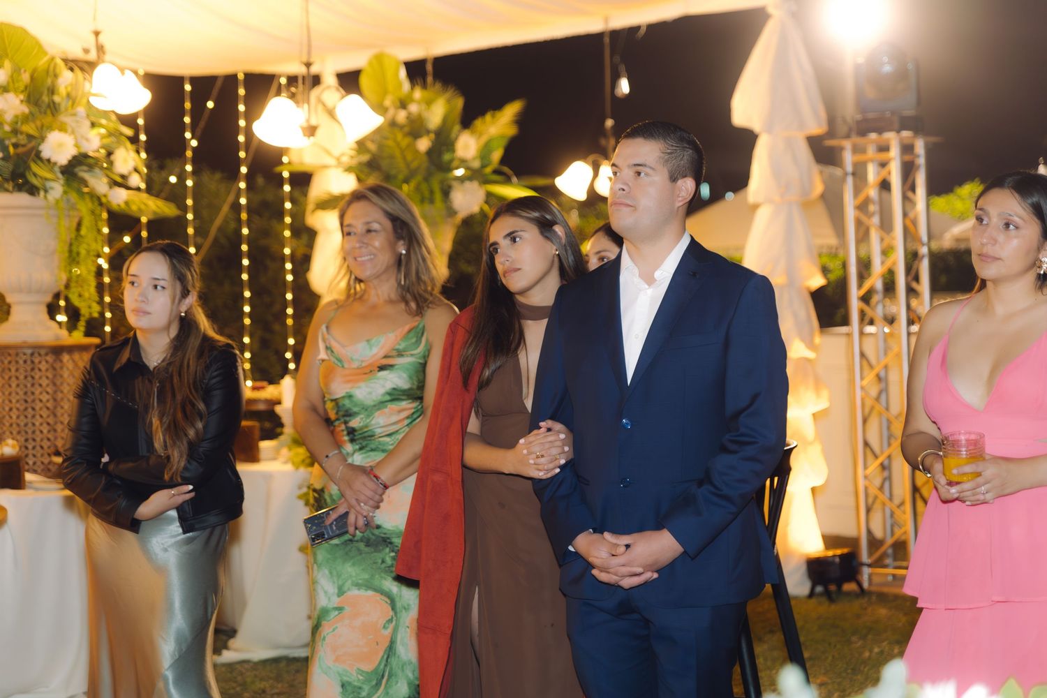 Wedding guests in formal attire gather and watch during an elegant outdoor evening wedding celebration.