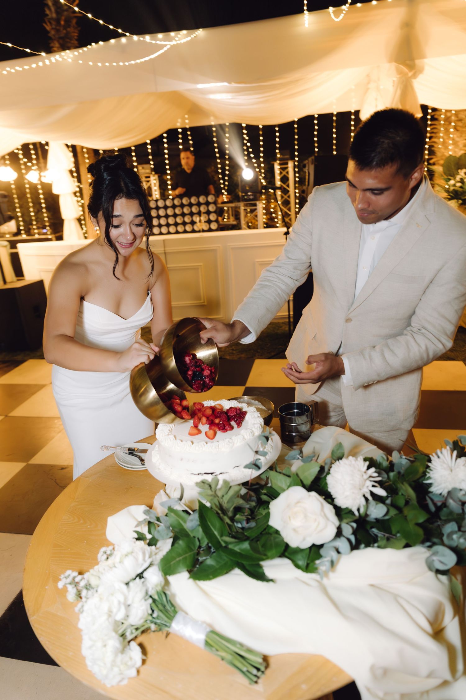 Bride and groom prepare to cut white wedding cake topped with fresh berries at elegant reception.