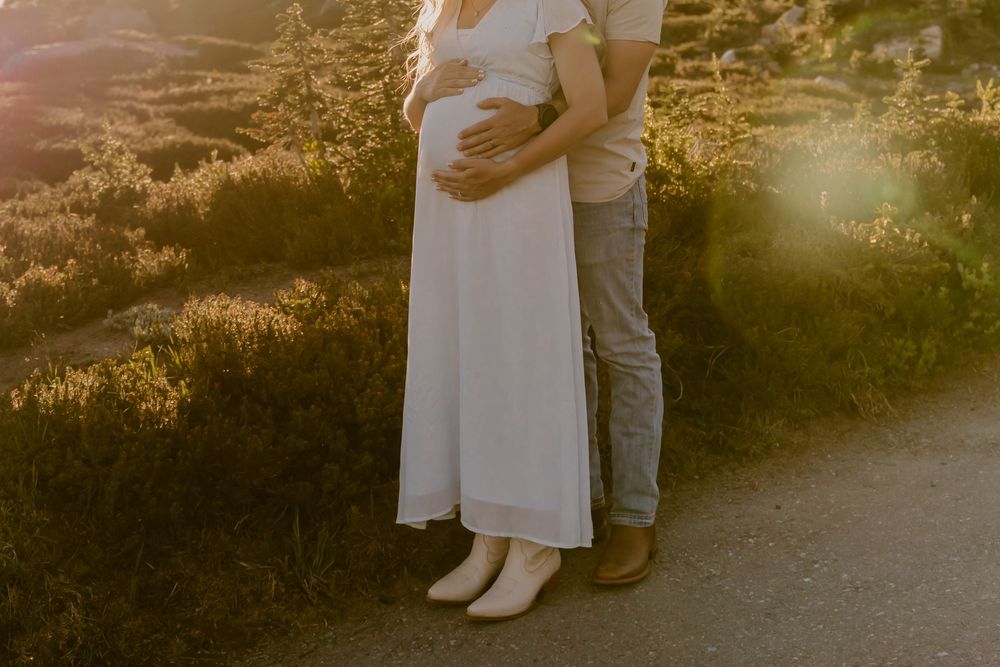 Couple embracing pregnant belly in warm sunset light on scenic mountain trail.