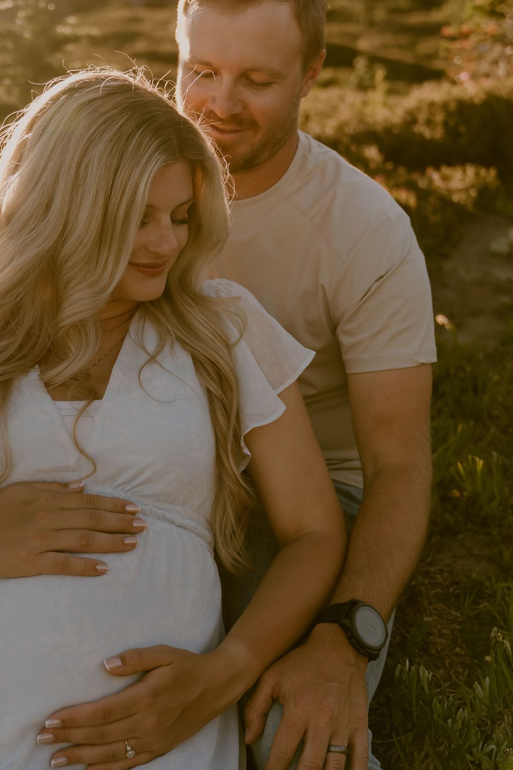 Couple tenderly holding pregnant belly during golden hour outdoor maternity photoshoot.