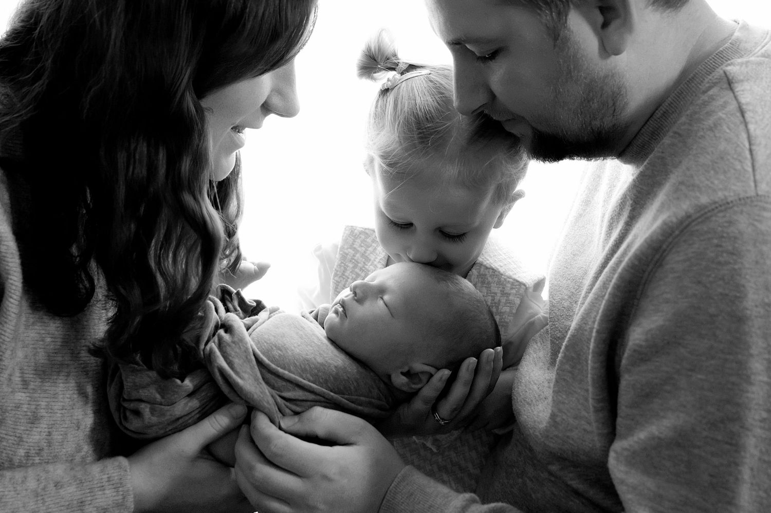 Black and white photo of a mother tenderly kissing her newborn baby, cradling the infant in her hands.