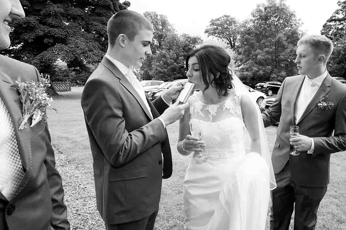 Black and white wedding photo of bride taking a shot from a hip flask at a wedding at Greenhill Hotel