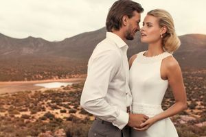 Elegant couple in wedding attire share intimate moment with scenic desert valley landscape behind them.
