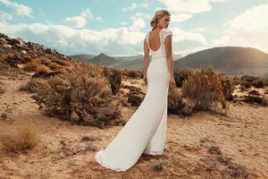 Woman in elegant white backless wedding gown poses in desert landscape with mountains in background.