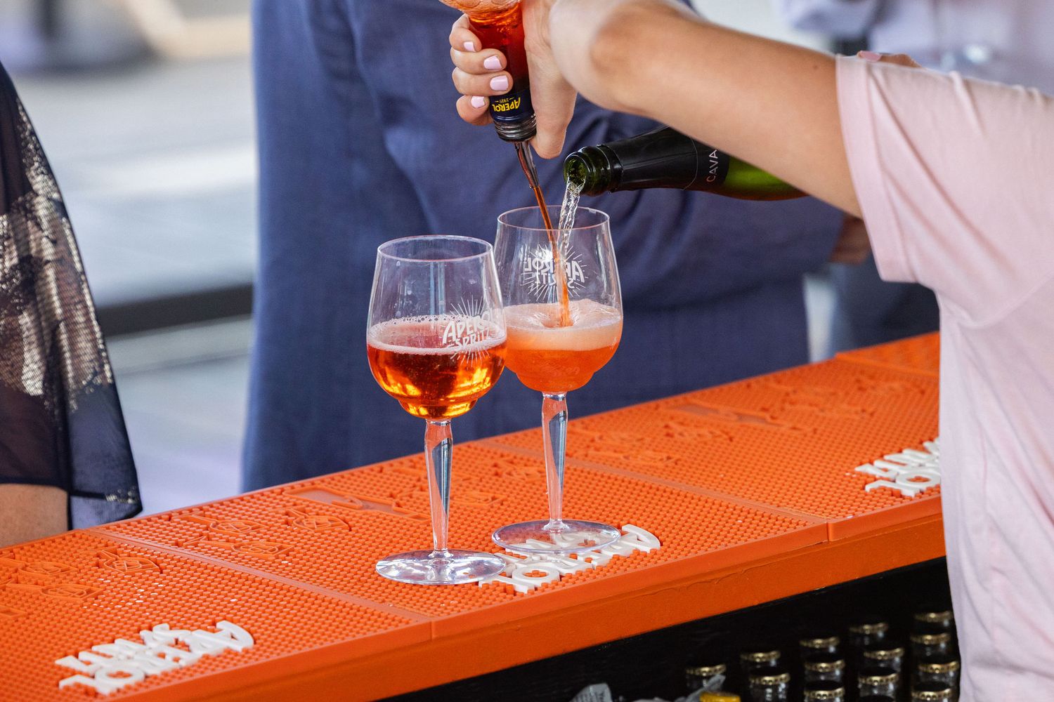 Bartender pouring sparkling rose wine into glasses on an orange table at an event.
