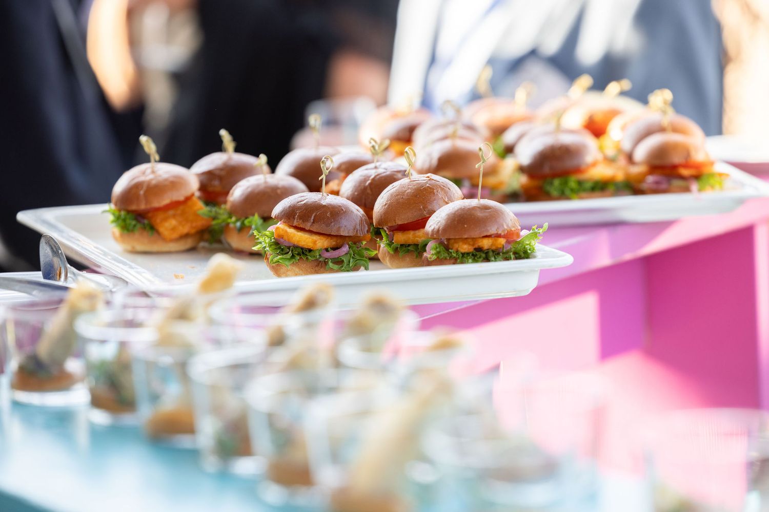 A catered event spread features gourmet mini sliders and appetizers displayed on a white serving tray.