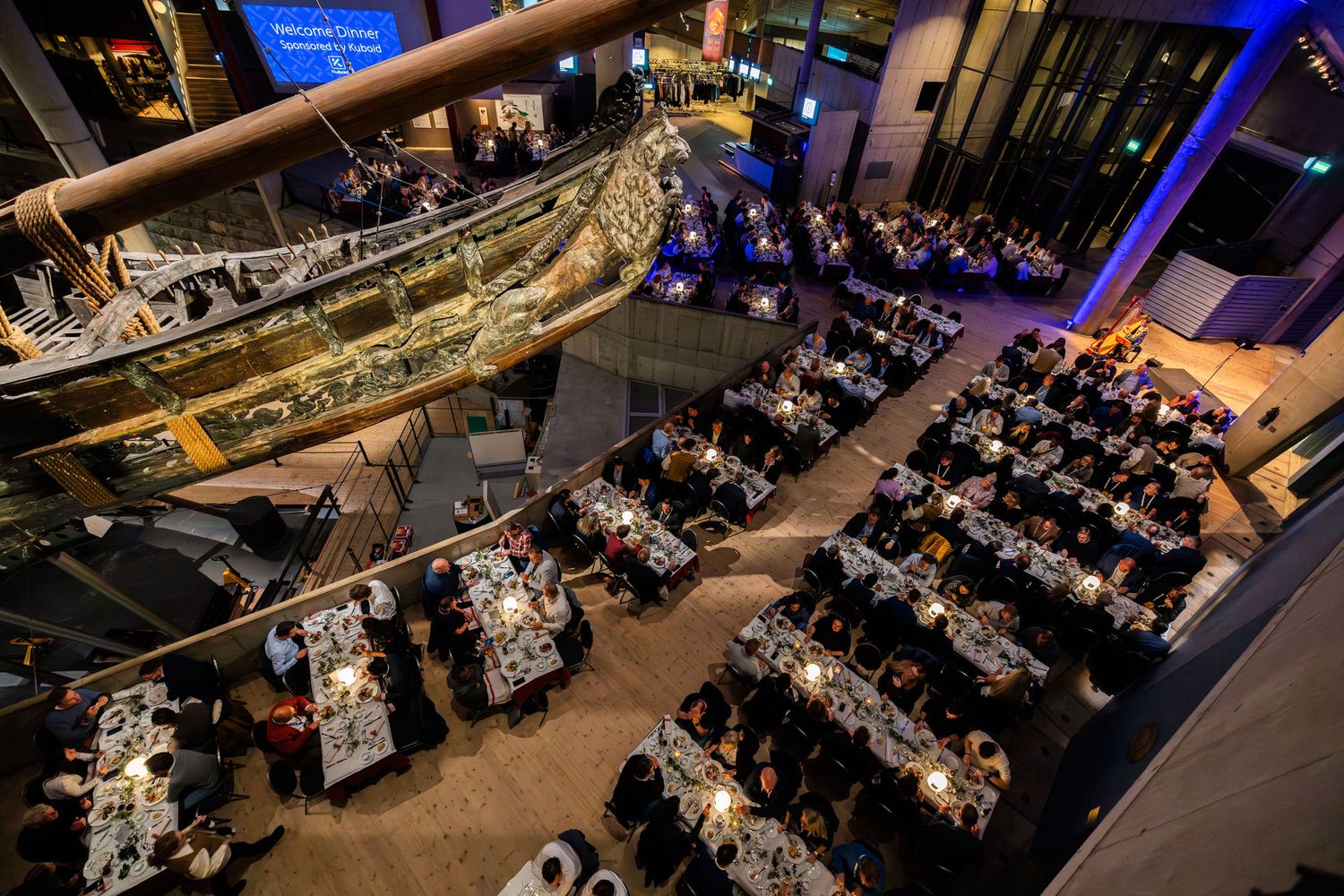 Aerial view of a formal gala dinner event inside a museum with a historic ship suspended overhead.