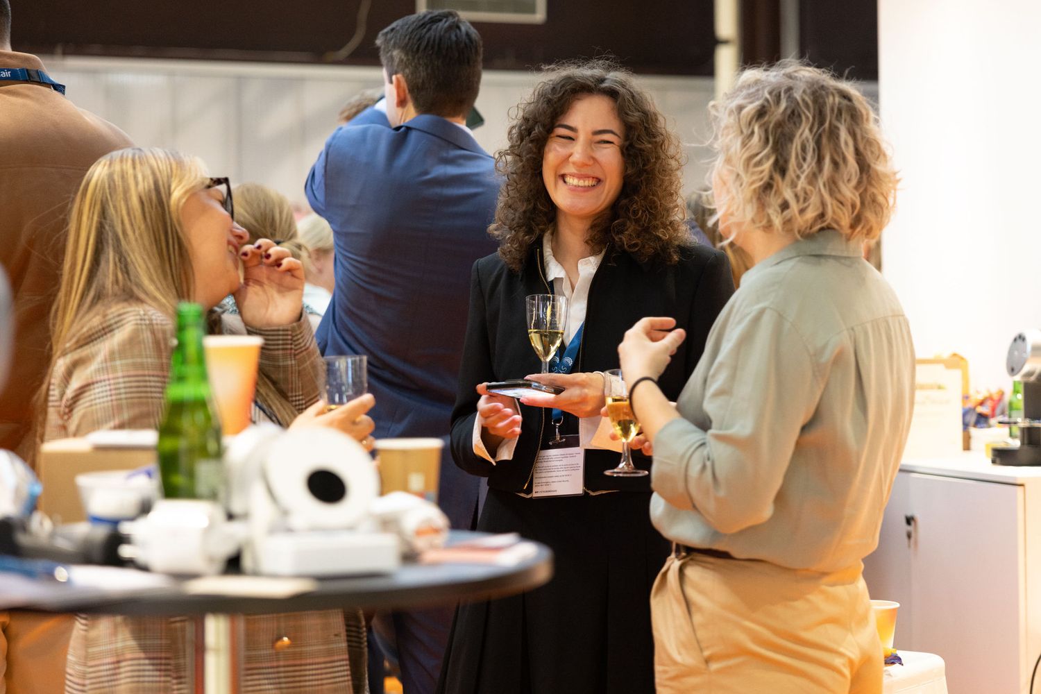 Three women laughing and socializing at a professional networking event with drinks.