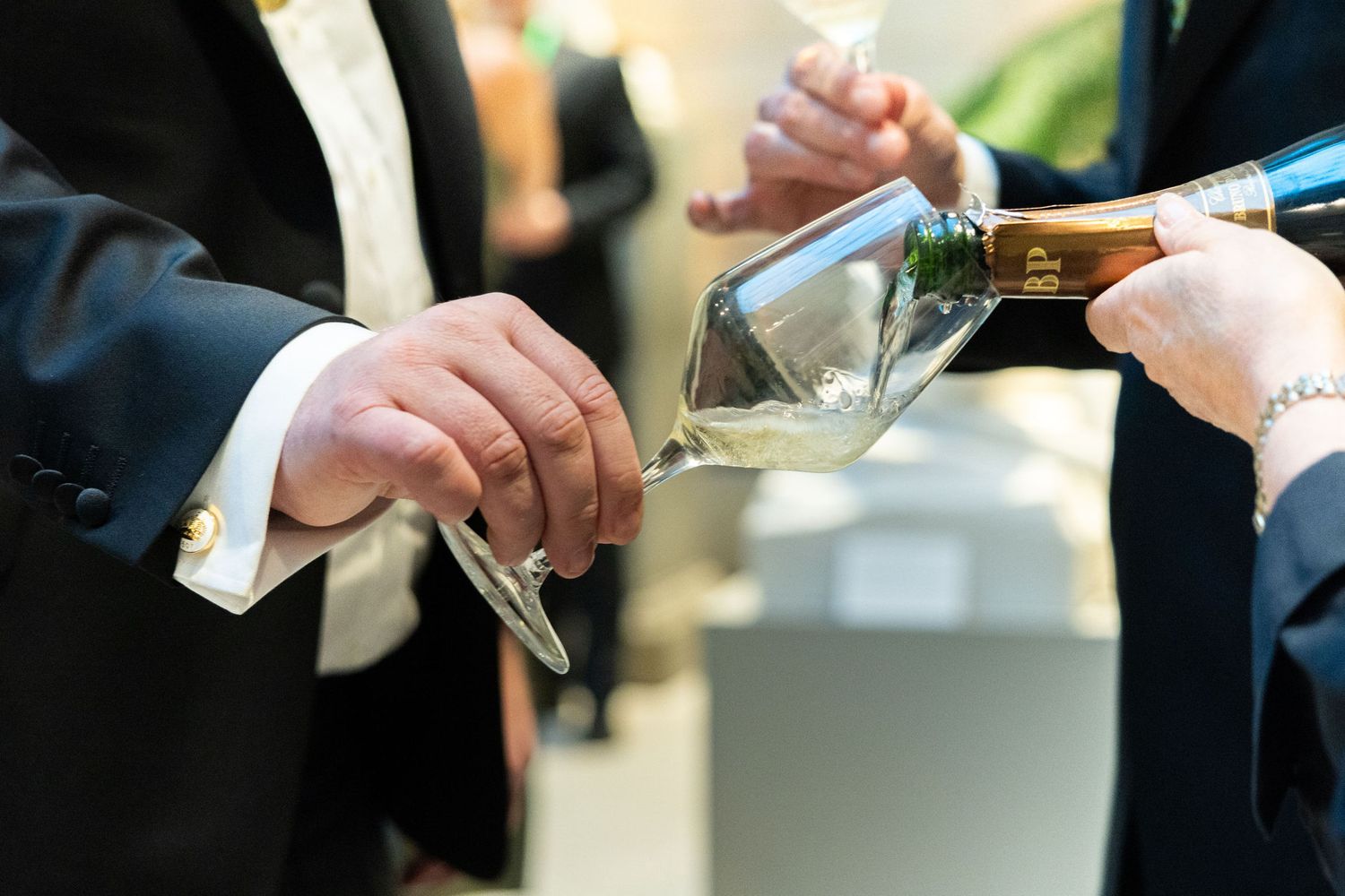 Formal server pouring white wine into a tilted glass at an elegant catered event.