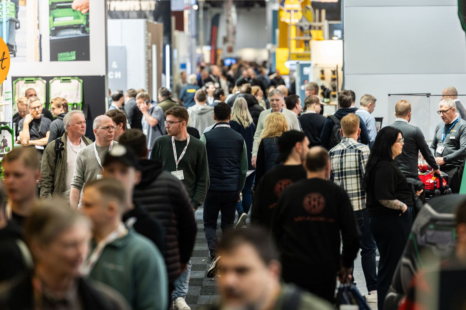 Large crowd of visitors walking through a busy trade show exhibition hall with vendor booths.