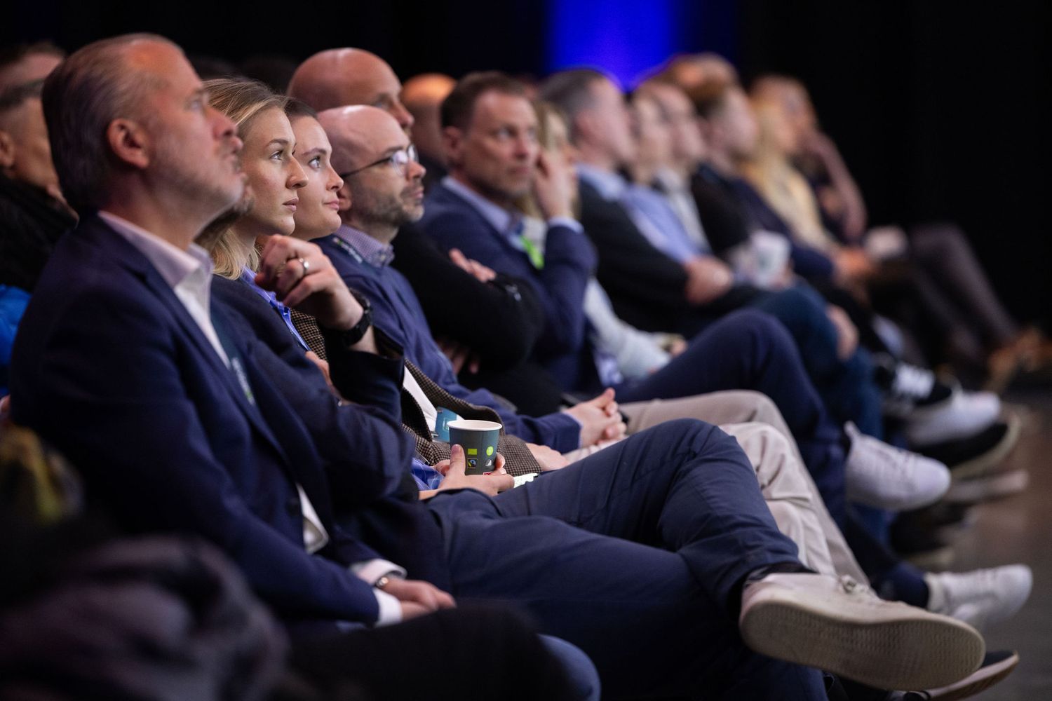 Business professionals in suits attentively watch a presentation at a corporate conference event.