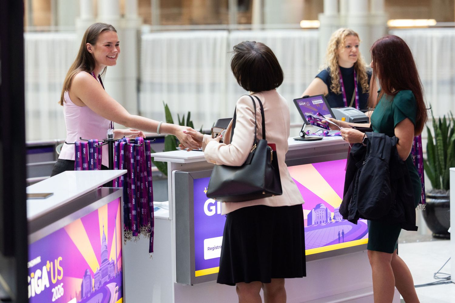 Registration desk staff assist attendees at a purple-branded conference event check-in counter.