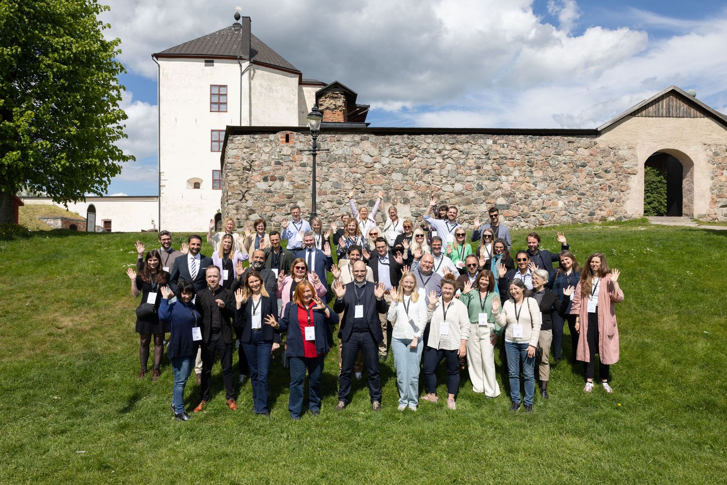 Large group of conference attendees posing outdoors near a historic stone castle on a sunny day.