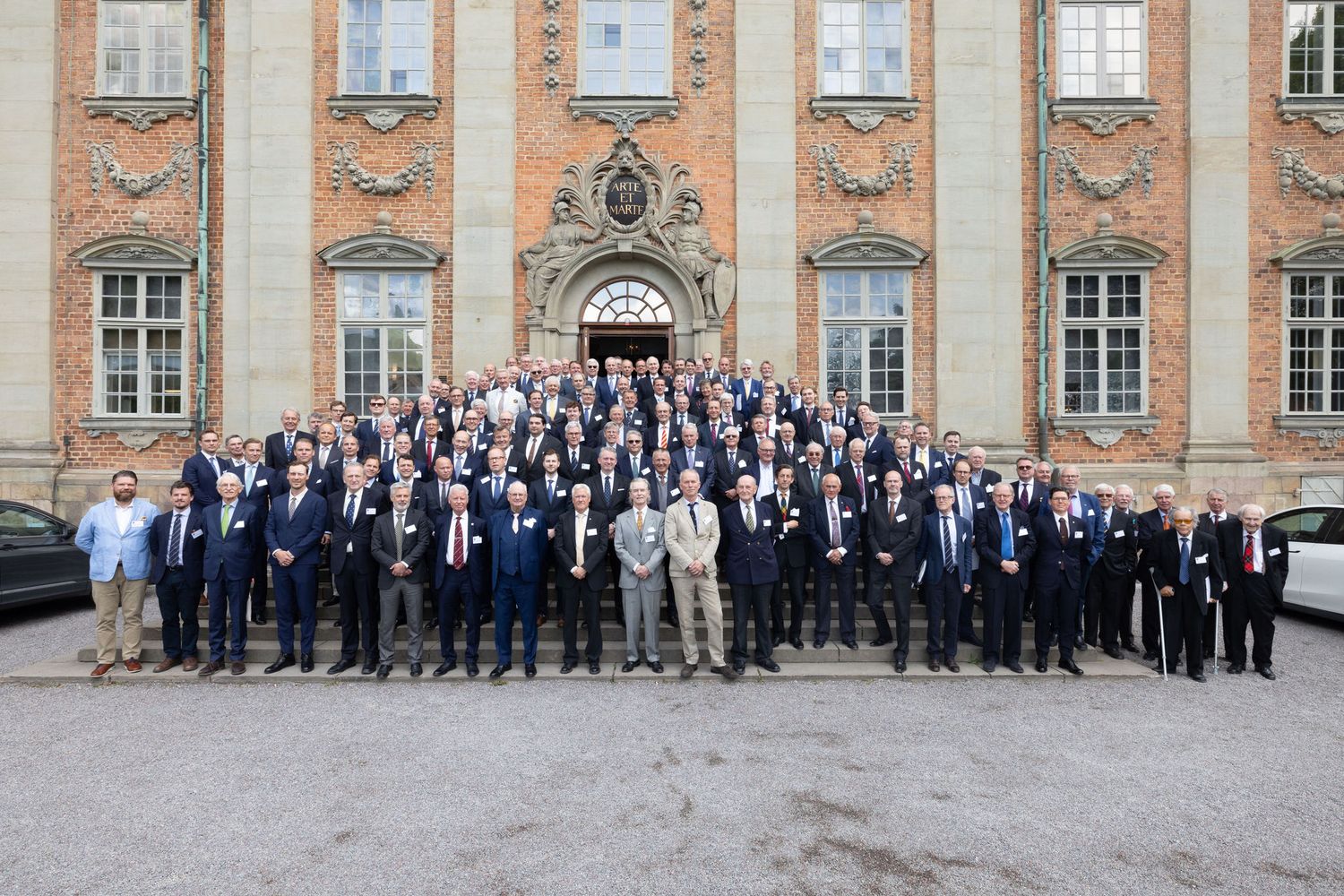 Large group of business professionals posing for a formal photo outside a historic brick building.
