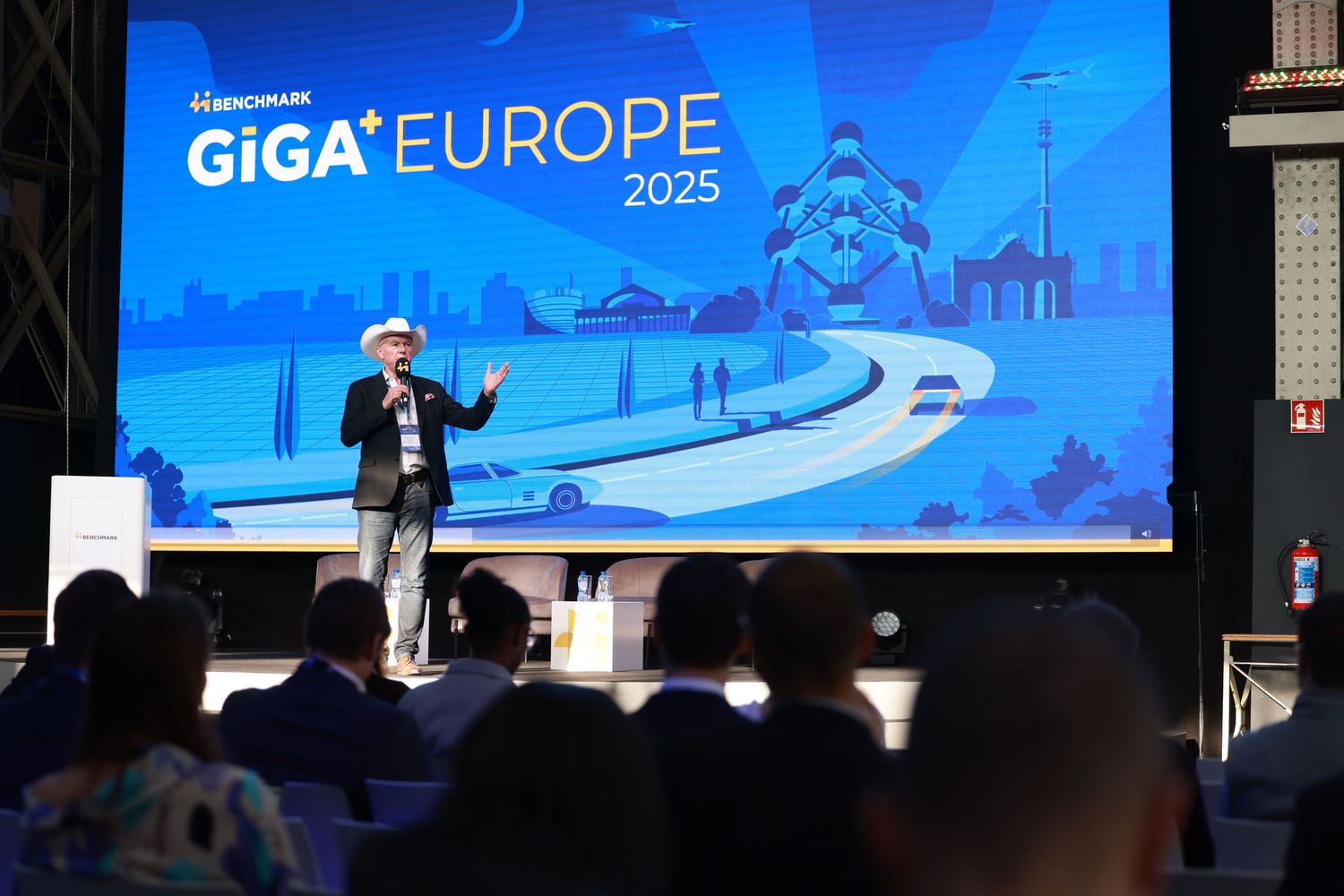 Speaker presenting on stage at GiGA Europe 2025 conference in front of a large branded screen.