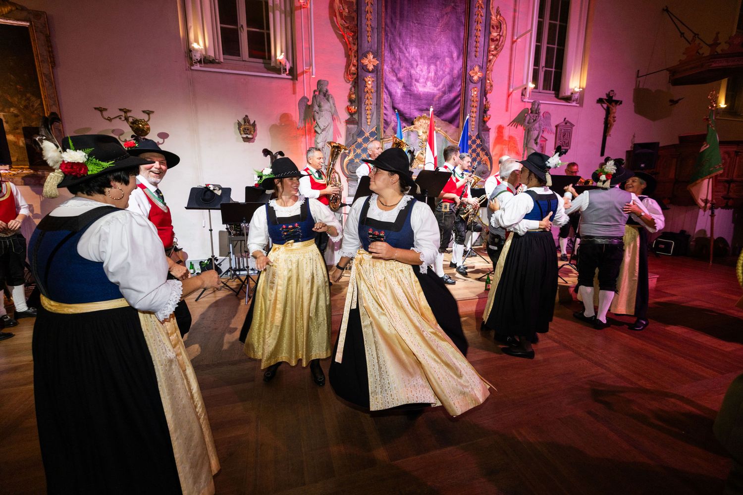 Performers in traditional folk costumes dance in a beautifully decorated hall during a cultural celebration event.