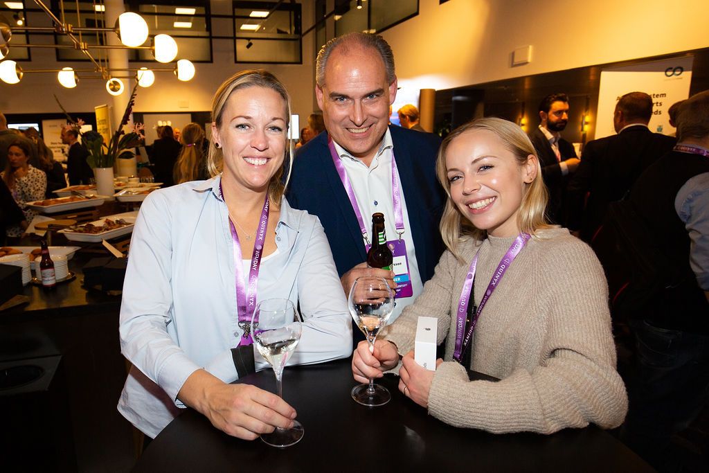 Two women and a man smile together holding wine glasses at a professional networking event.