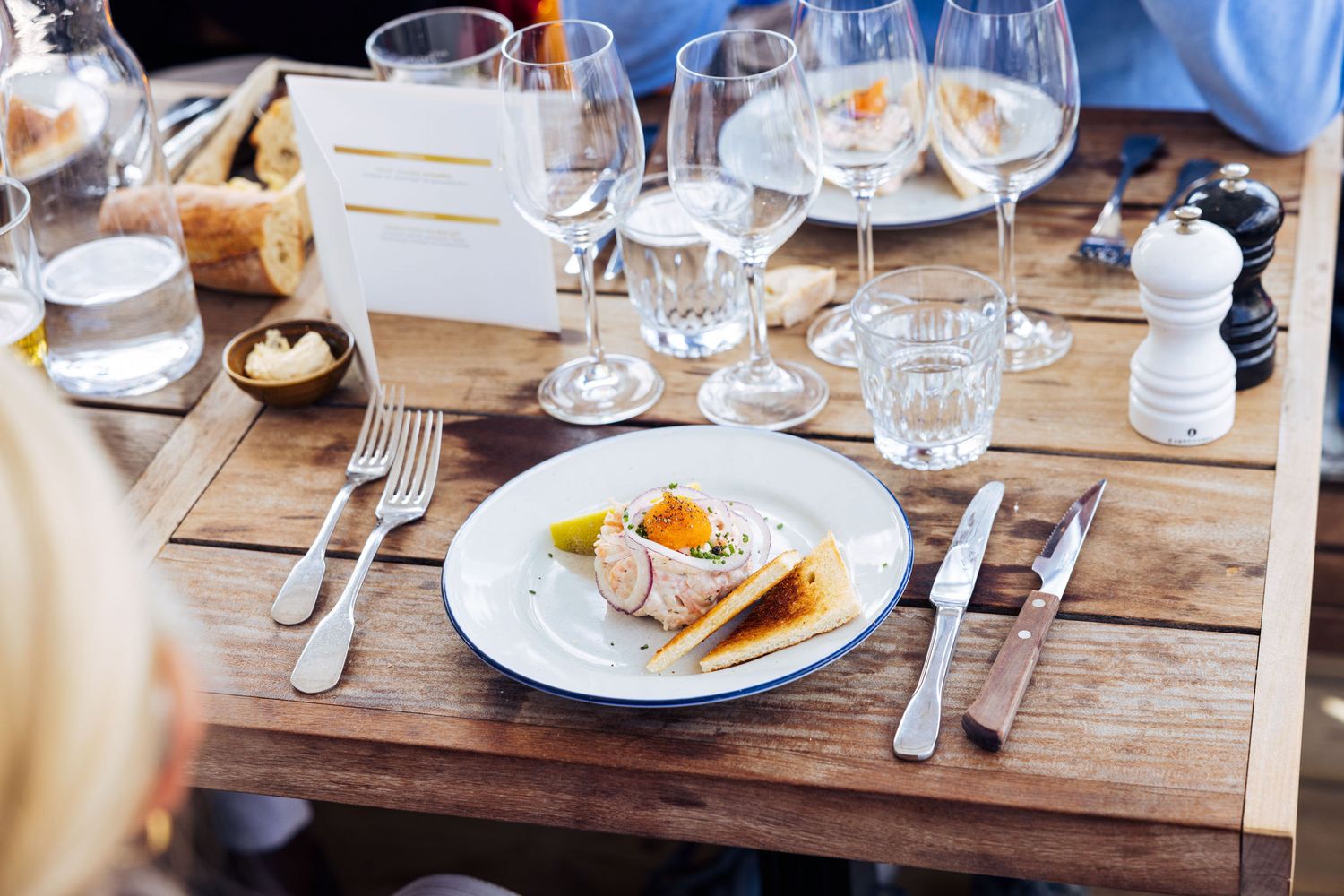 Elegant restaurant table setting with gourmet dish, wine glasses, and wooden table at an upscale dining establishment.
