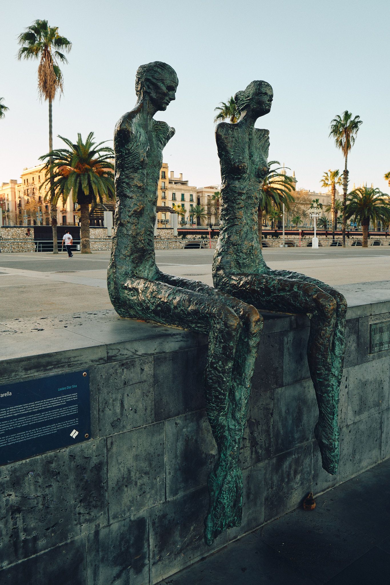 White platform sneakers standing on El Port de Barcelona sign on dark textured ground.