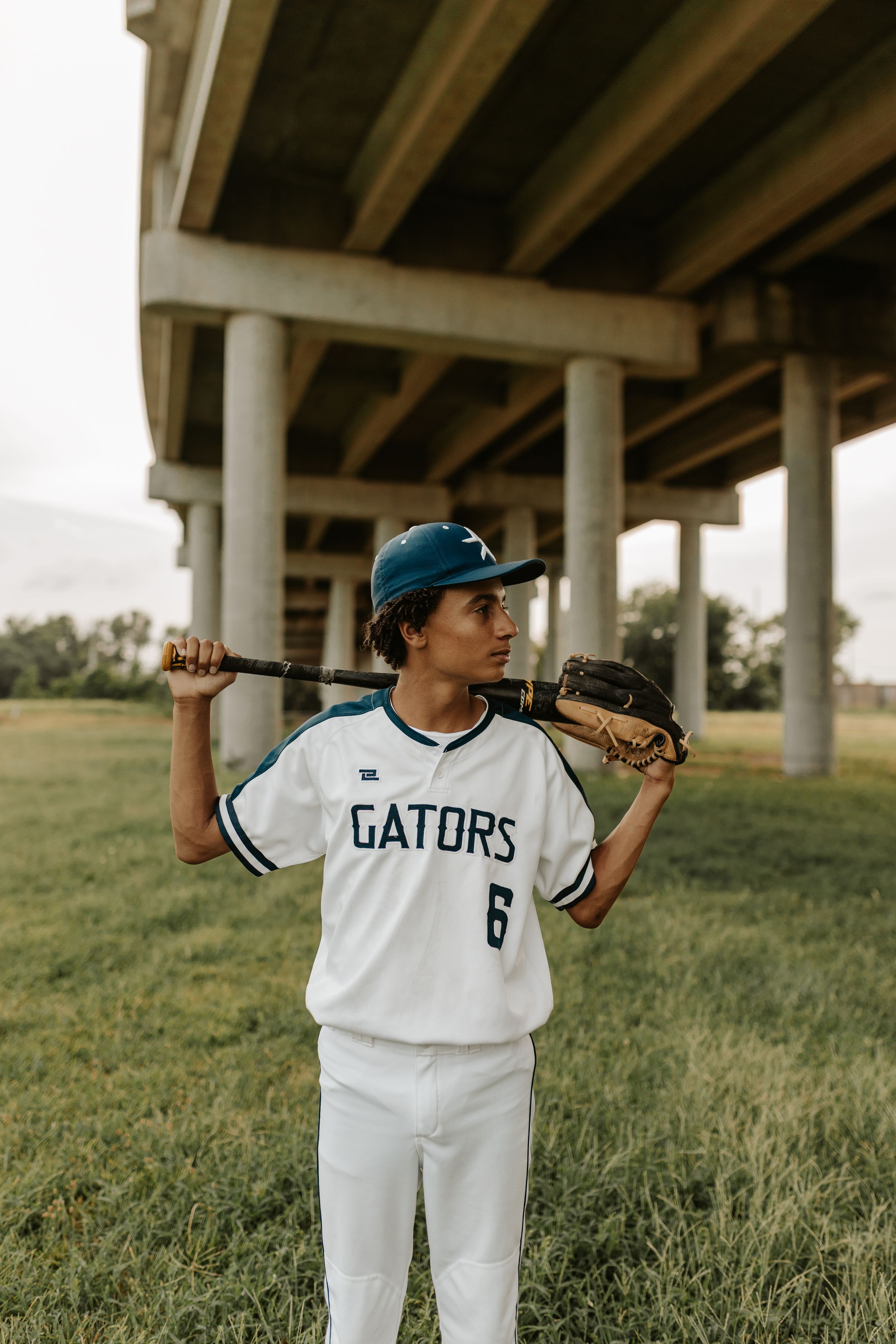 Baseball player in Gators #6 jersey holds bat behind shoulders under a bridge.