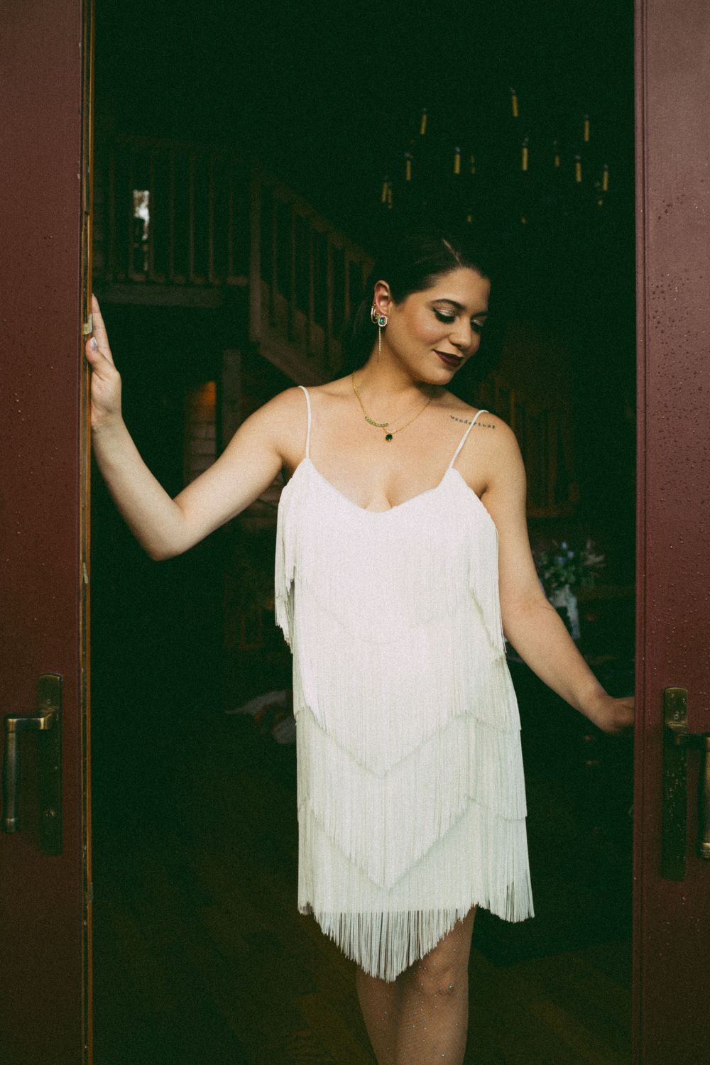 Woman in white fringe flapper dress posing in doorway of rustic venue.