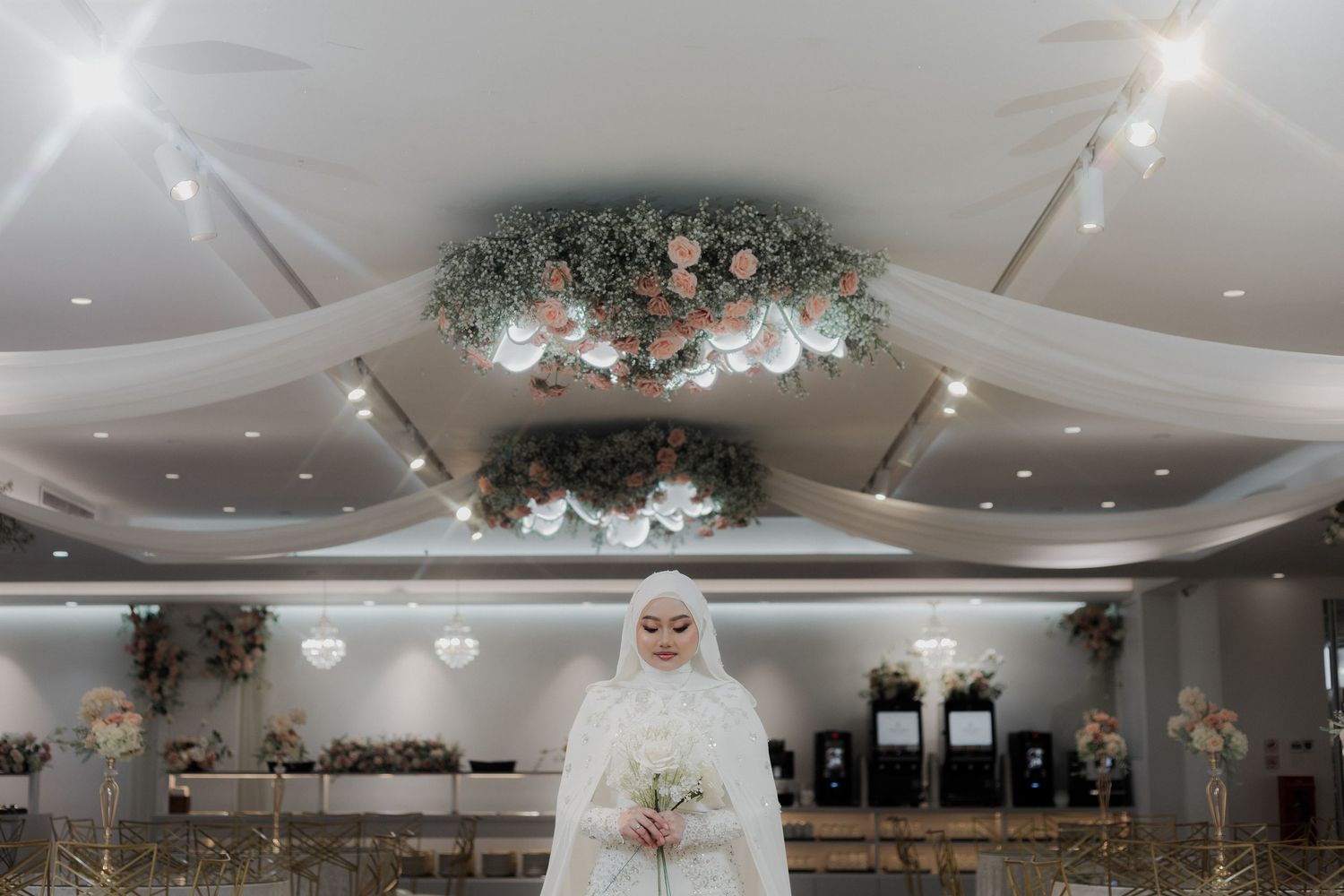 Muslim couple in traditional Javanese wedding attire sitting together at an outdoor ceremony with floral decorations and ocean view.
