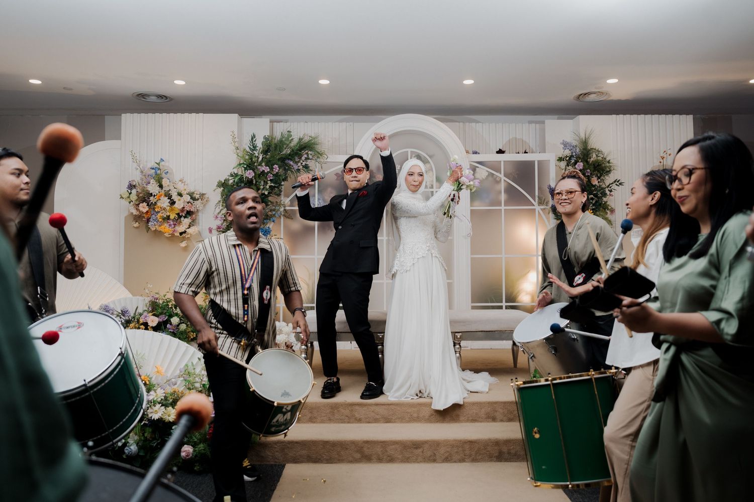 Wedding couple celebrates with live drummers and musicians in elegant indoor ceremony venue.