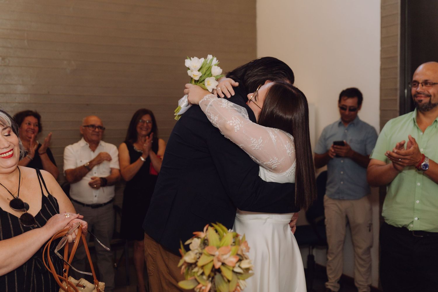 Bride and groom embrace as wedding guests applaud and celebrate after ceremony.