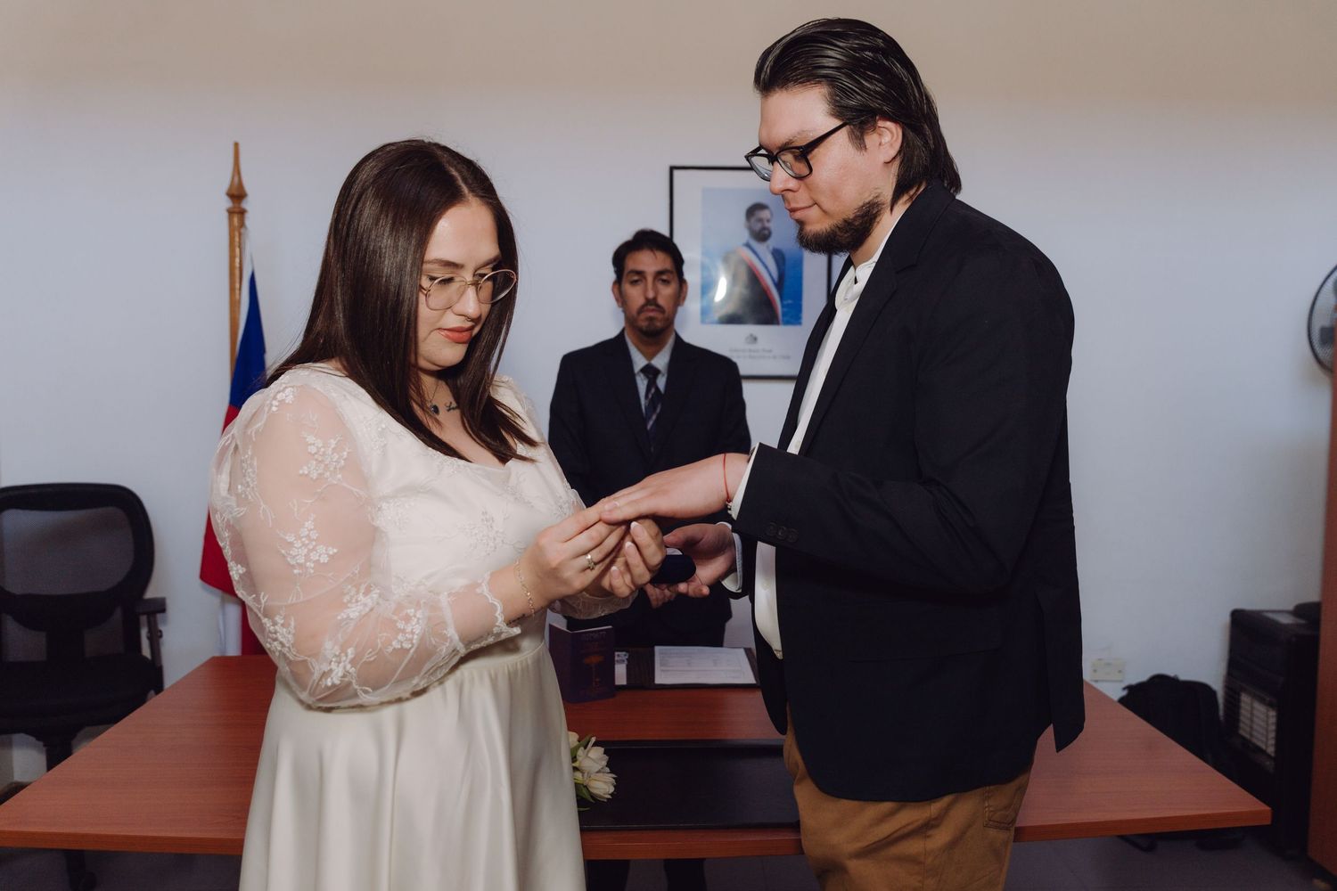 Groom places wedding ring on brides finger during civil ceremony with officiant.
