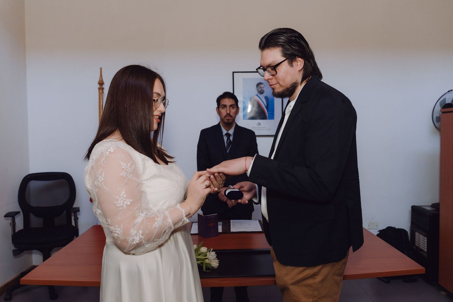Couple exchanges wedding rings before officiant at civil marriage ceremony indoors.