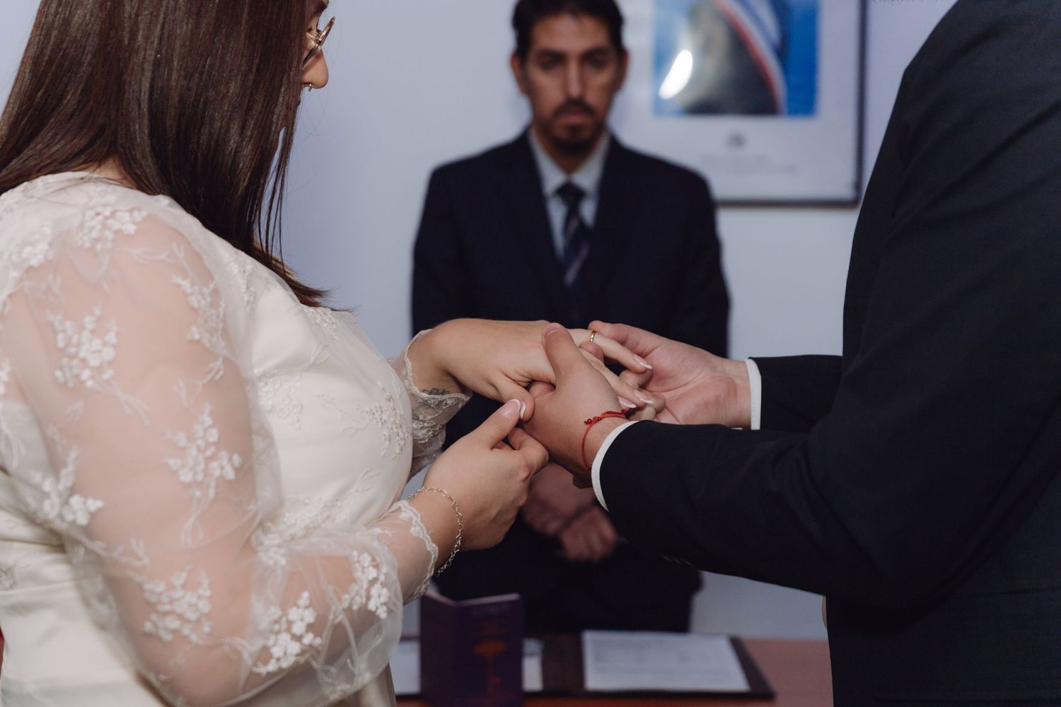 Close-up of couple exchanging wedding rings with officiant visible in background.