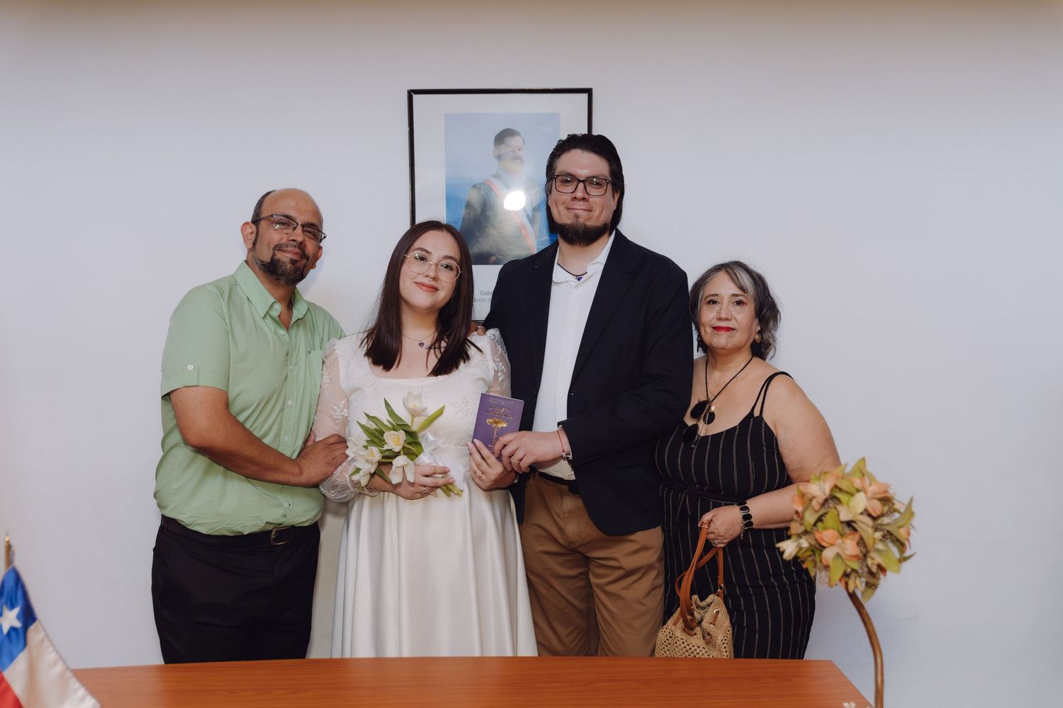 Bride and groom pose with family members at a civil wedding ceremony with a Chilean flag in the background.