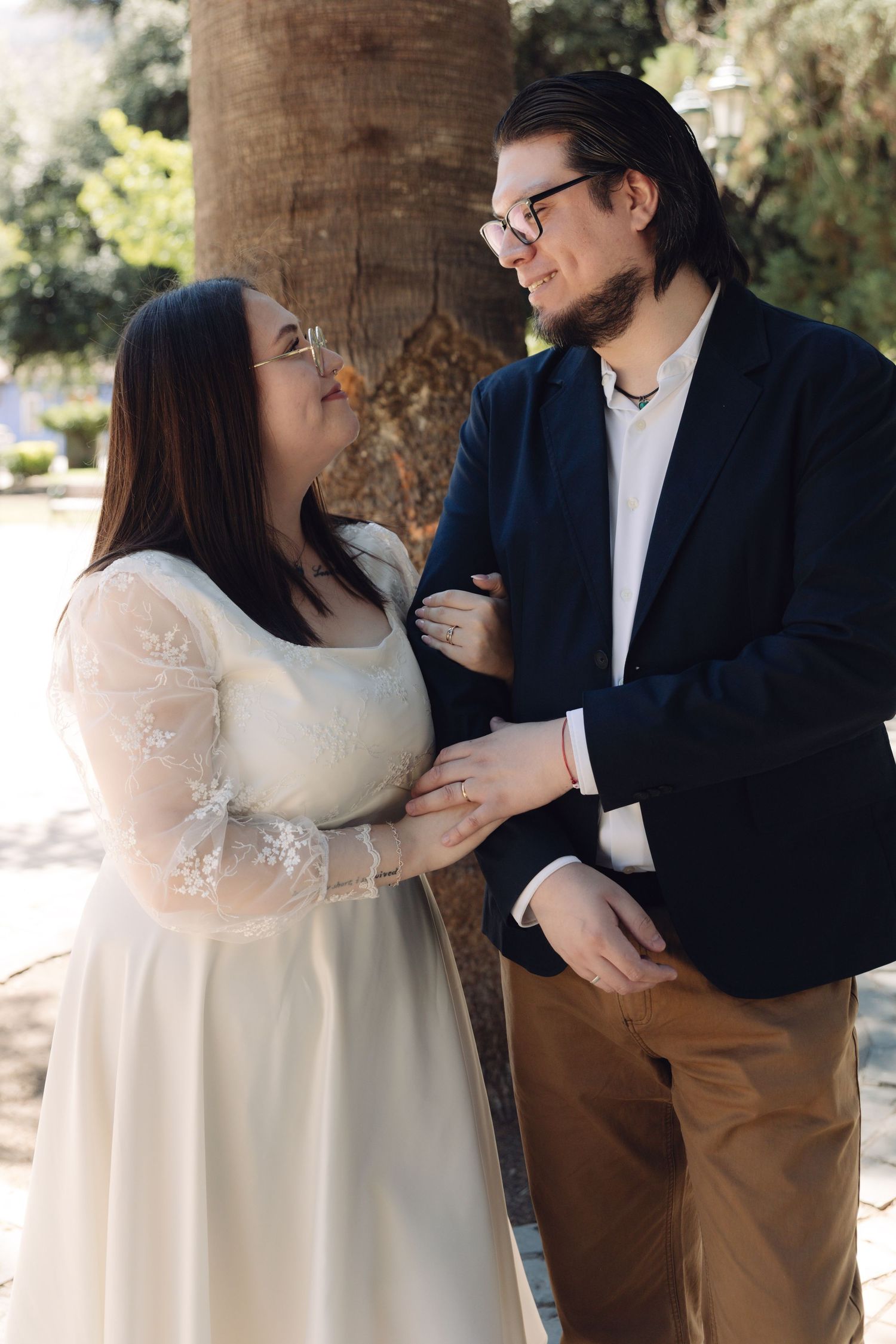 Bride and groom sharing a loving gaze while standing together near a park tree.