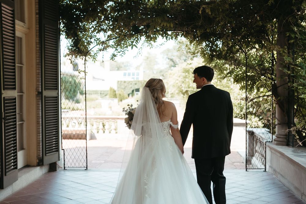 Bride and groom walking hand in hand on a sunlit venue terrace, bride wearing a flowing white gown with veil.