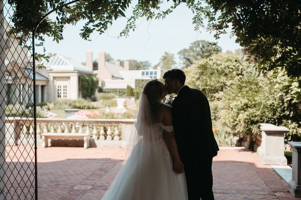 Bride and groom share a romantic kiss in silhouette on a brick terrace at an elegant estate wedding venue.