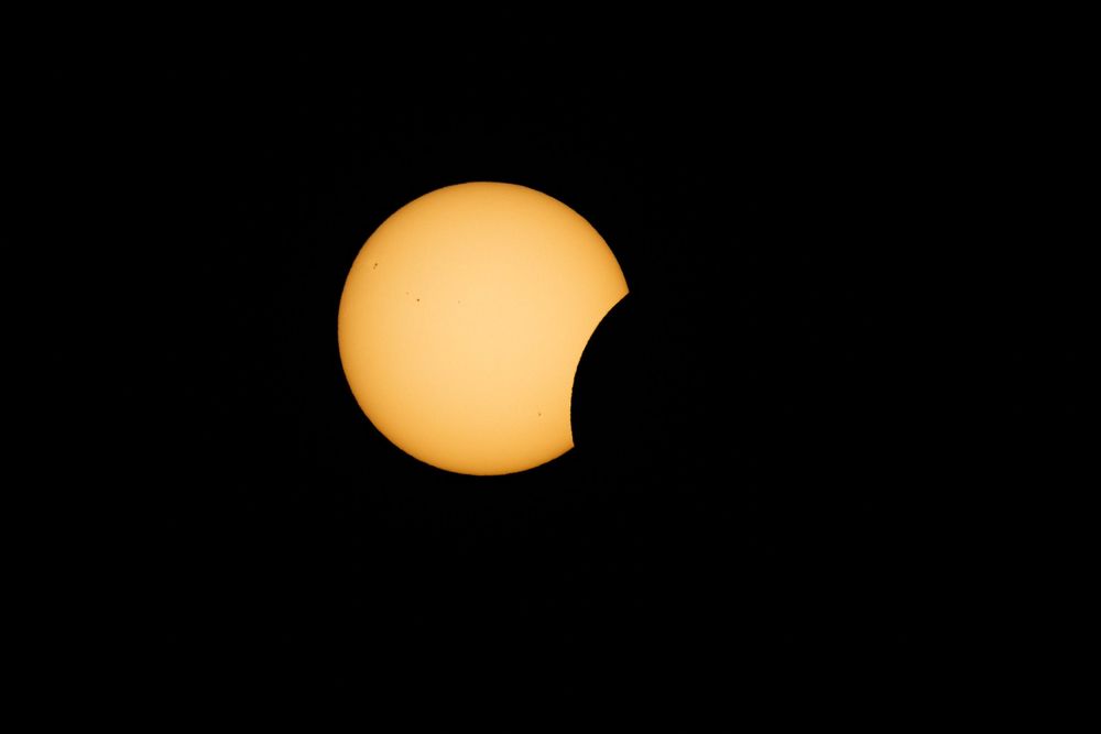 Partial solar eclipse with moon beginning to cover the sun against a black sky.
