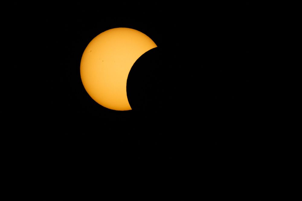 Partial solar eclipse with the moon covering part of the glowing orange sun against a dark black sky.