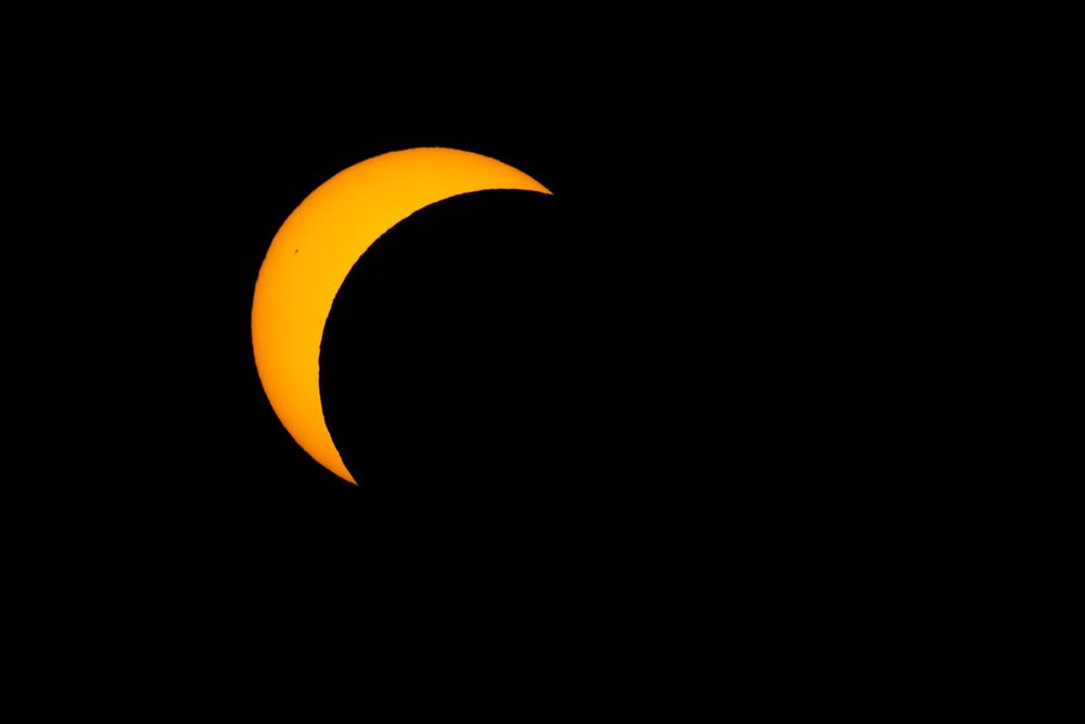 Crescent sun during partial solar eclipse with moon covering most of the sun on black background.