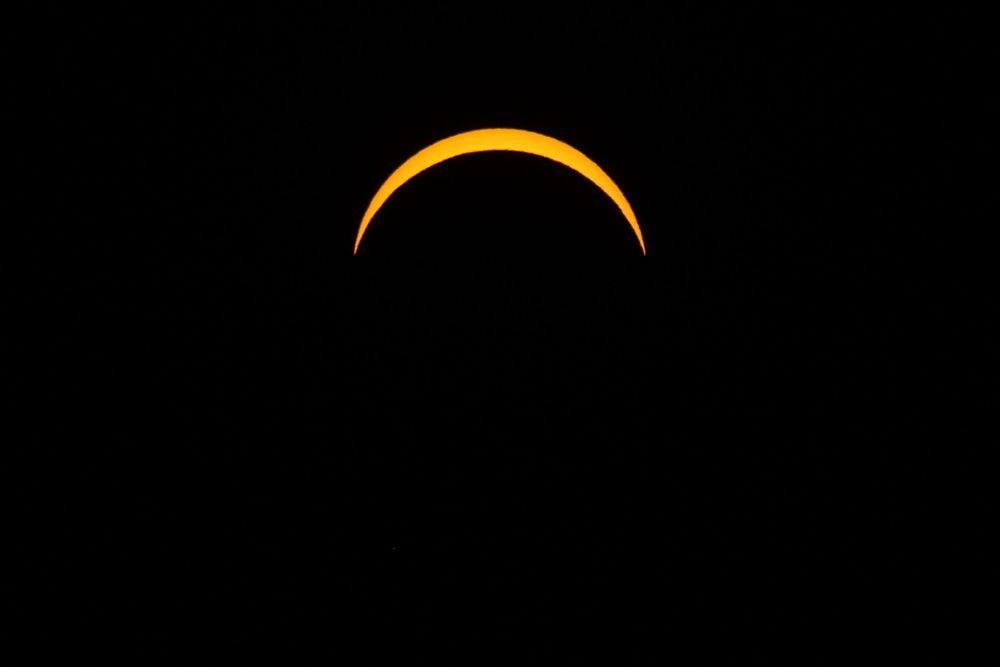 A stunning solar eclipse crescent glowing in brilliant orange against a pitch-black sky.