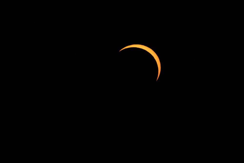 A stunning annular solar eclipse glowing orange against a dark black sky, showing a crescent ring of fire effect.