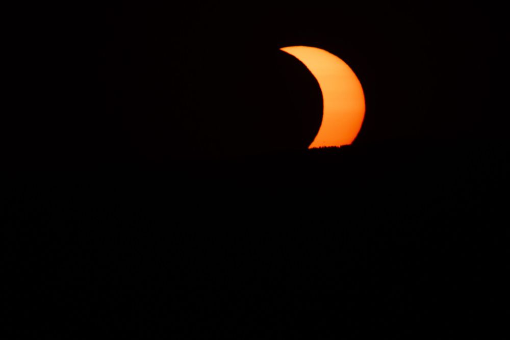 Partial solar eclipse with crescent sun glowing orange against a dark black sky.