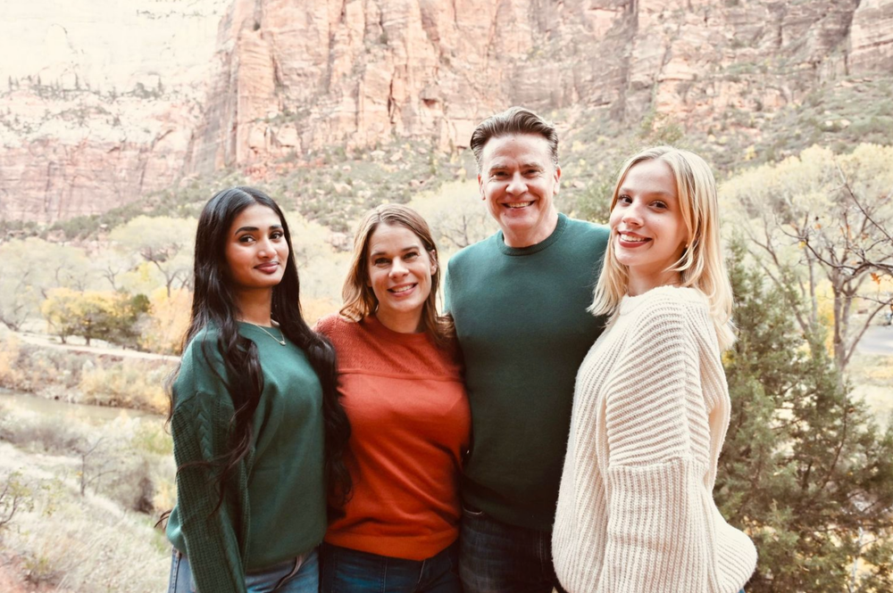 Four smiling people pose together outdoors with stunning red rock canyon scenery in the background.