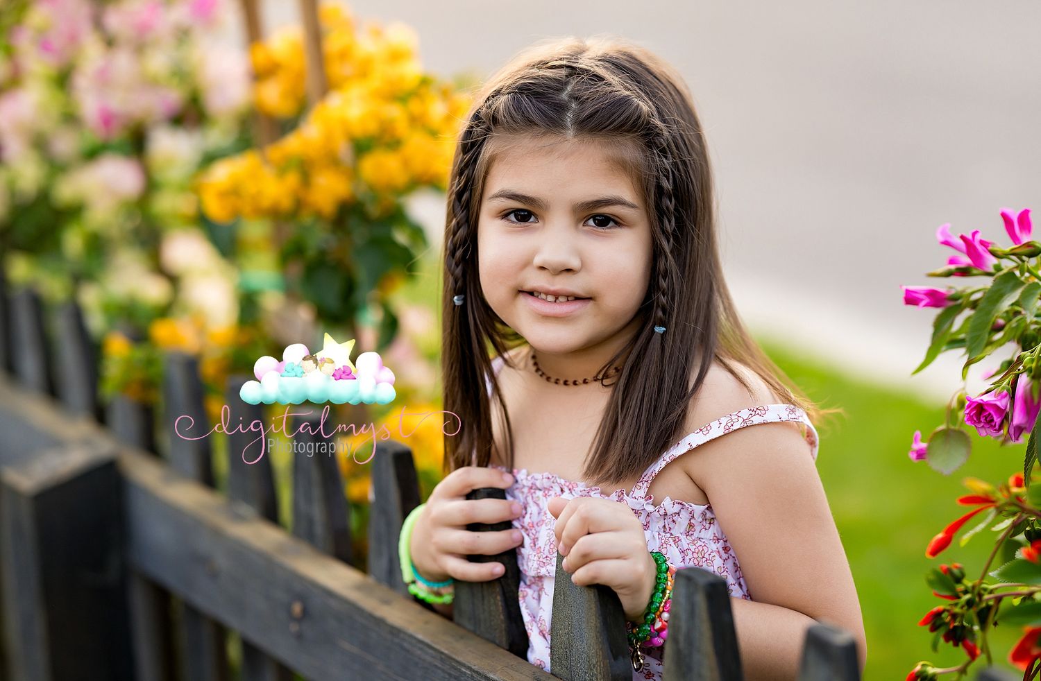 Young girl with braided hair smiling by a wooden fence surrounded by colorful flowers in a garden.