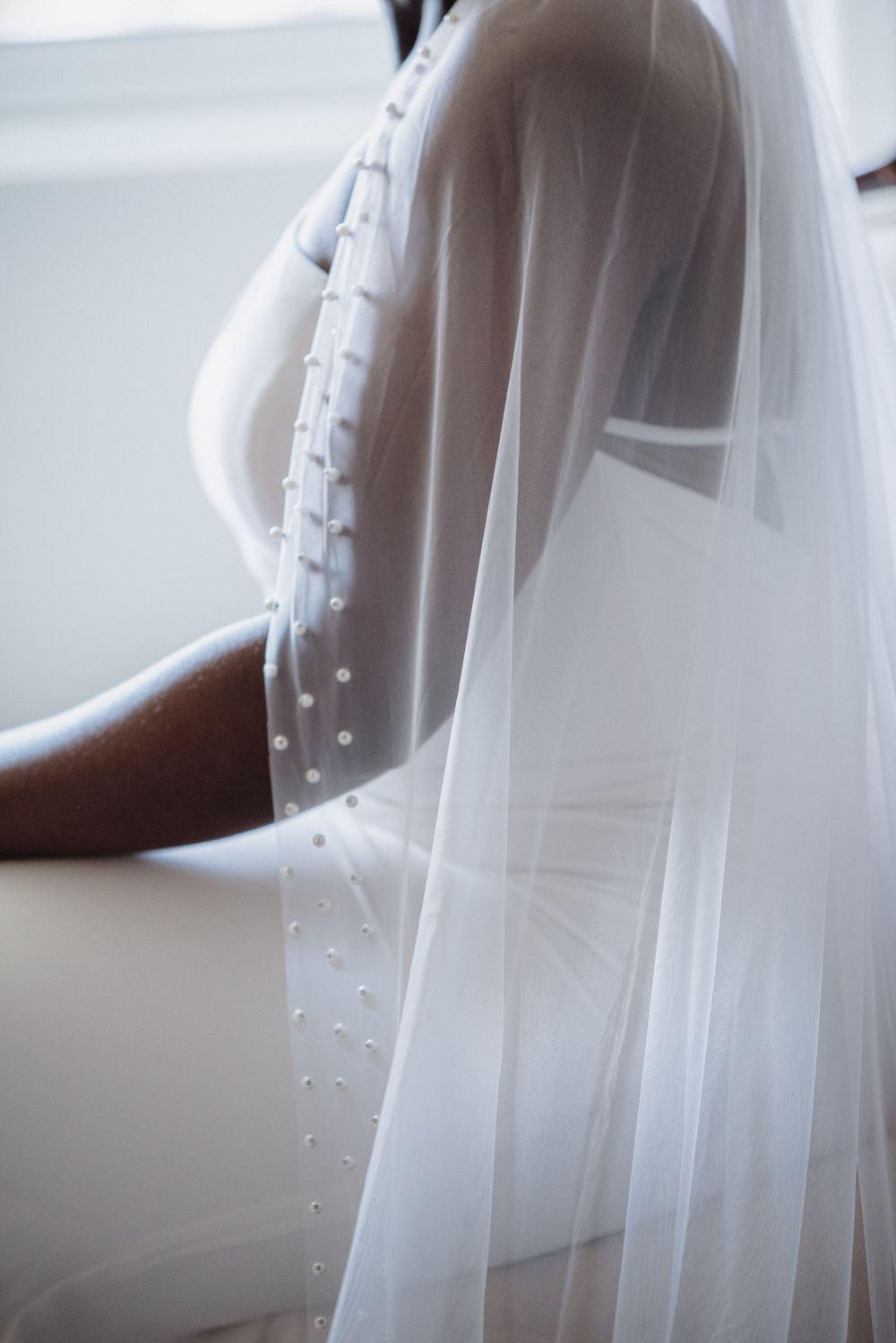 Detailed shot of a wedding dress sleeve with delicate pearl buttons and flowing veil.