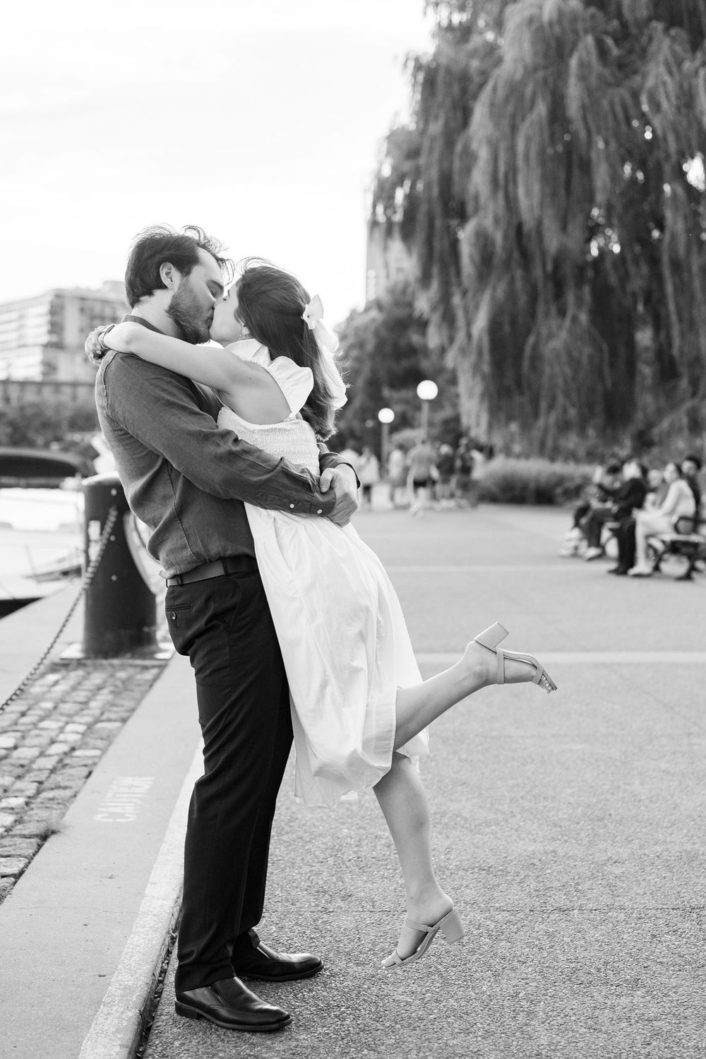 Black and white photo of a couple sharing a romantic kiss outdoors, woman lifting her leg gracefully.