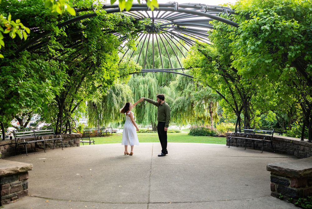 Couple dancing under a lush green iron pergola archway in a scenic garden park.