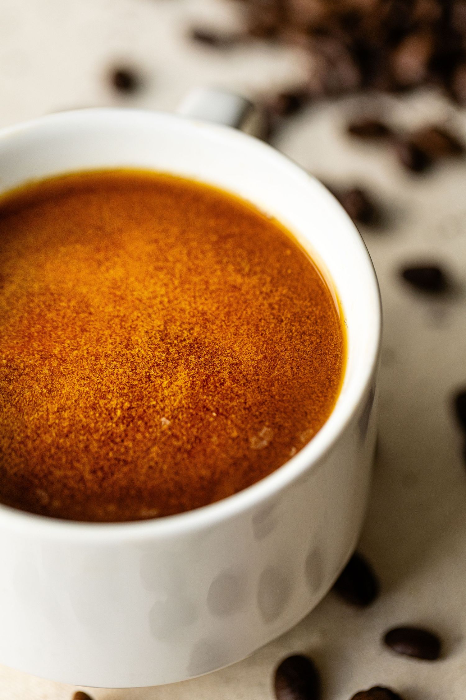 Close up shot of a vibrant cup of coffee in a white ceramic cup against a burlap table setting.