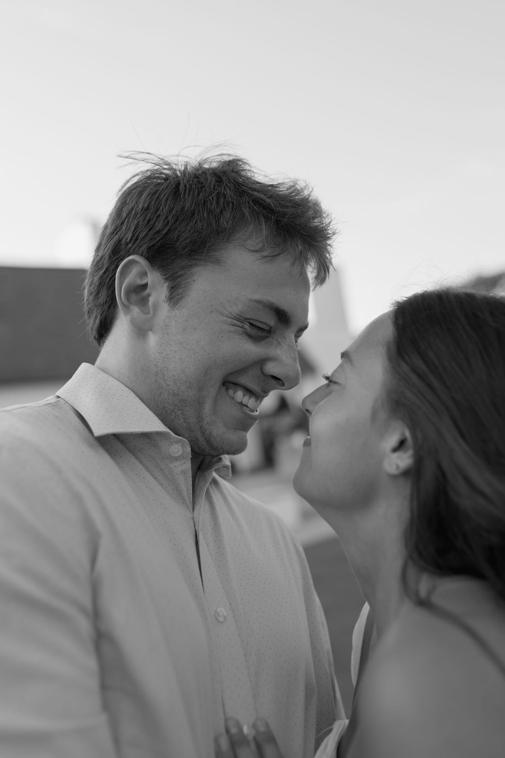 Black and white photo of a laughing couple sharing a romantic moment, the woman leaning in to kiss the smiling man.