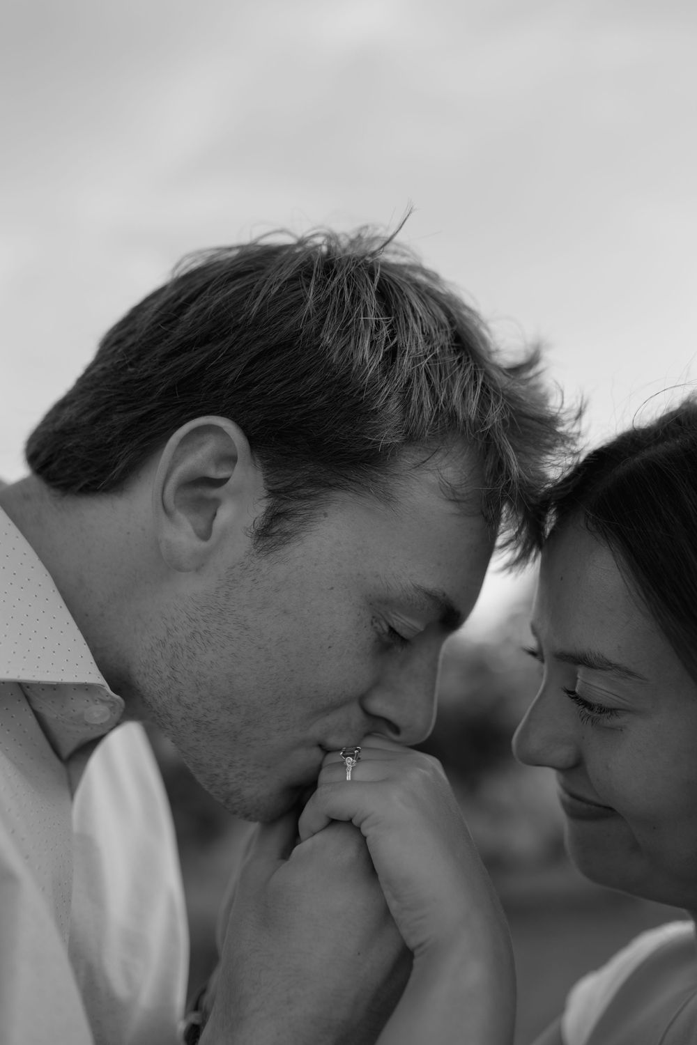 Black and white close-up of a groom kissing his brides hand while they lean their heads together tenderly.